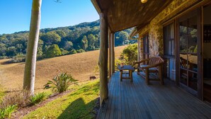 Une terrasse en bois avec une table et des chaises, donnant sur un champ et des collines boisées.