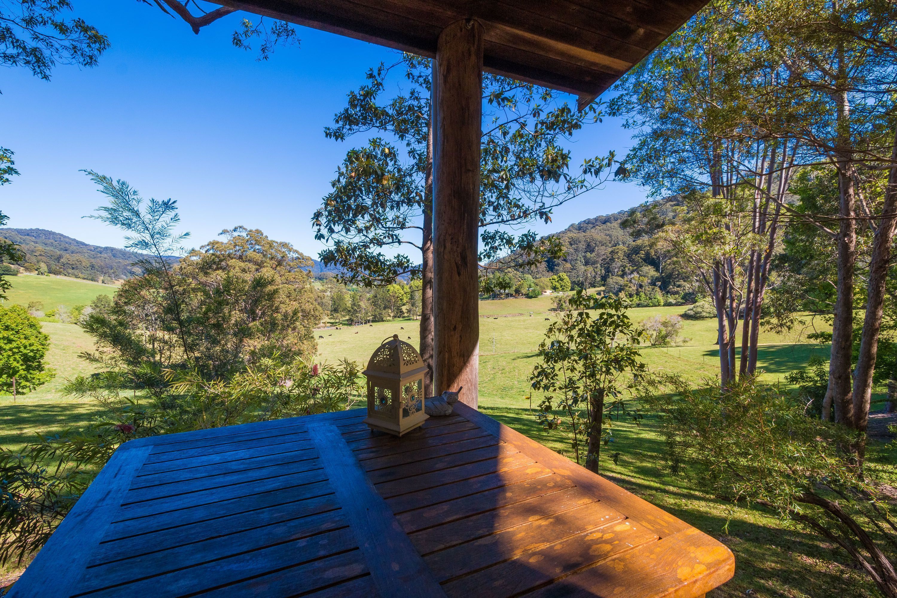 Une terrasse en bois, agrémentée d’une lanterne et d’un banc, offre une vue imprenable sur un paysage verdoyant, avec des arbres et des collines.