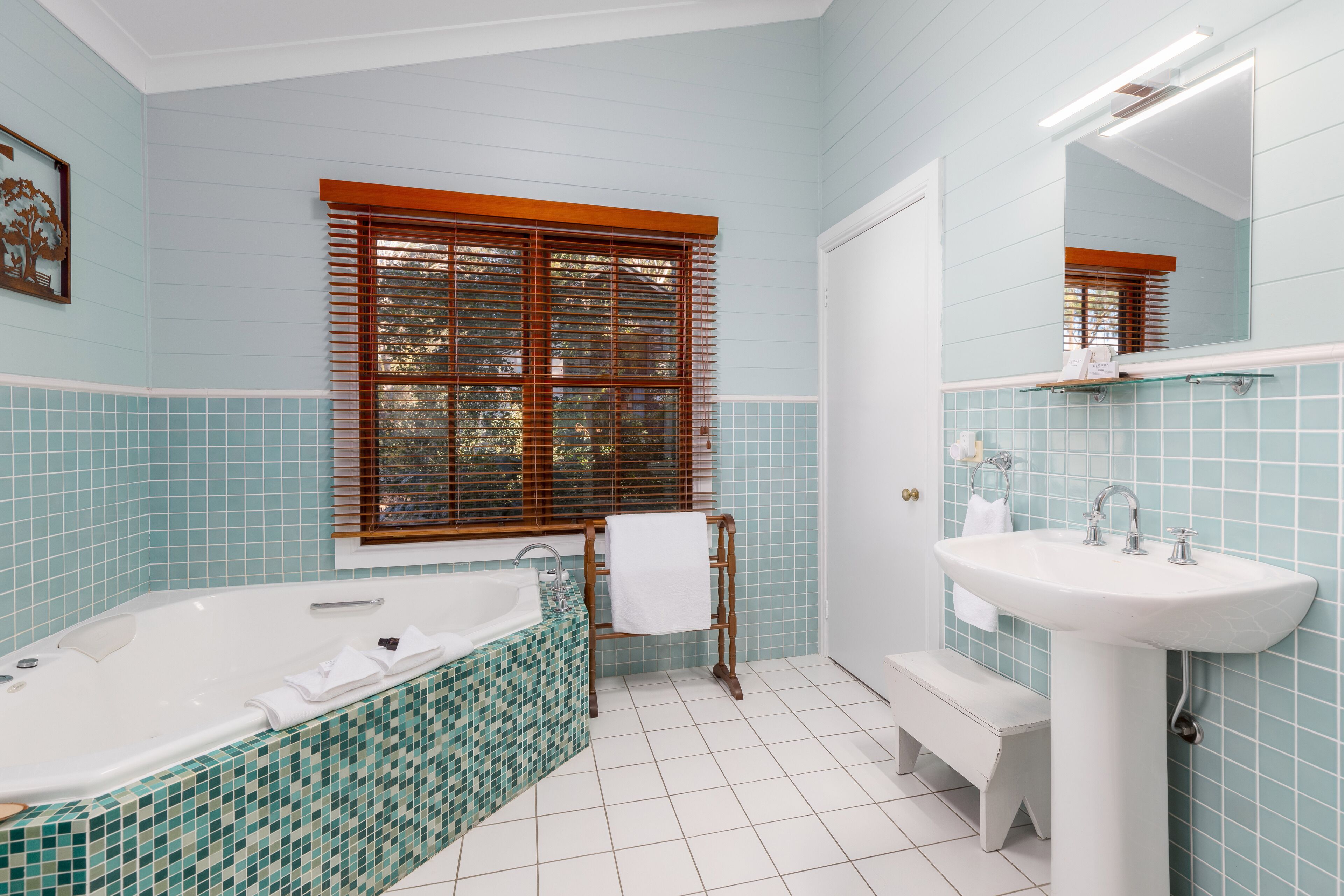 A bathroom with a bathtub, sink, and window with blinds.