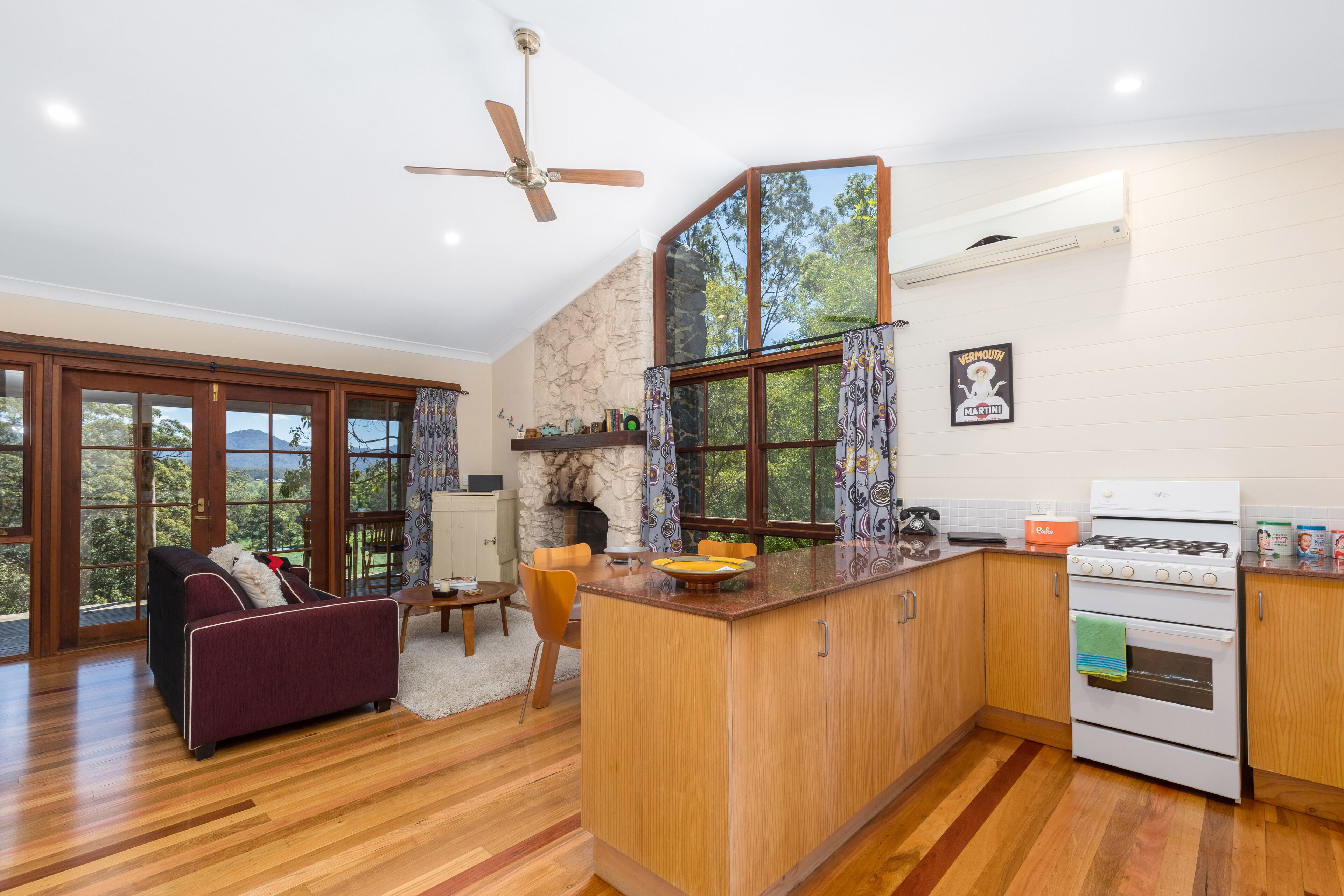 A spacious living area with a large window, a fireplace, and a kitchen with wooden cabinets and a stove.
