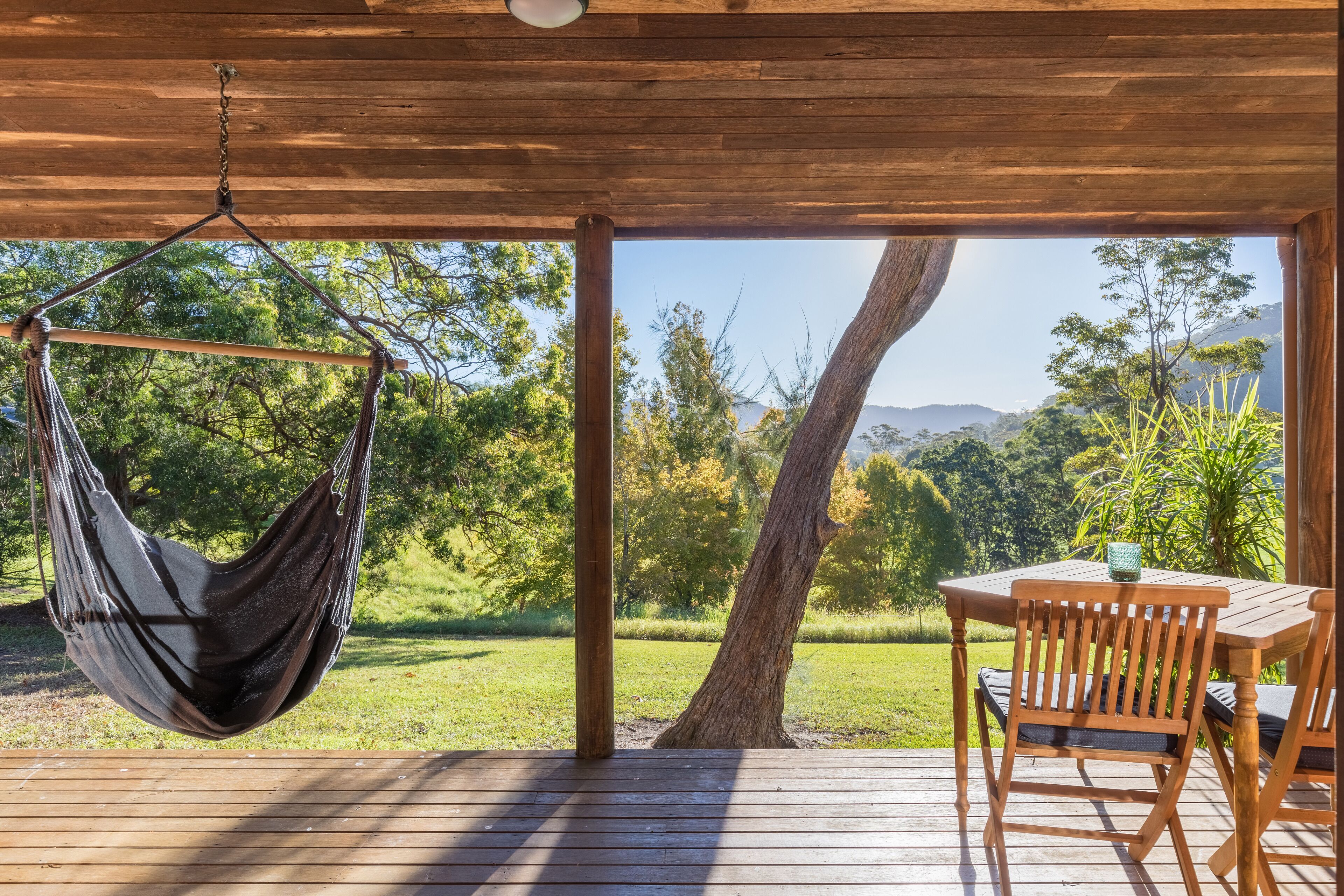 A wooden deck with a hammock and a table with chairs, overlooking a lush green landscape.