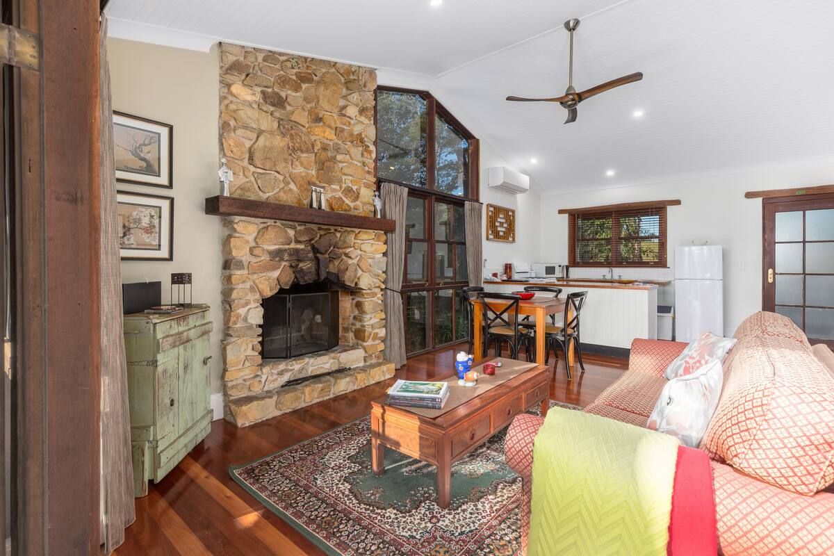 A cozy living room with a stone fireplace, wooden furniture, and a dining area with a view of the outdoors.
