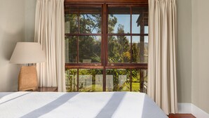 Une chambre avec une grande fenêtre, un lit, une table de chevet et une lampe.