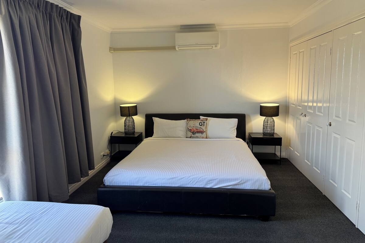 Habitación de hotel con una cama grande, dos mesitas de noche con lámparas, un armario y un equipo de aire acondicionado en la pared.
