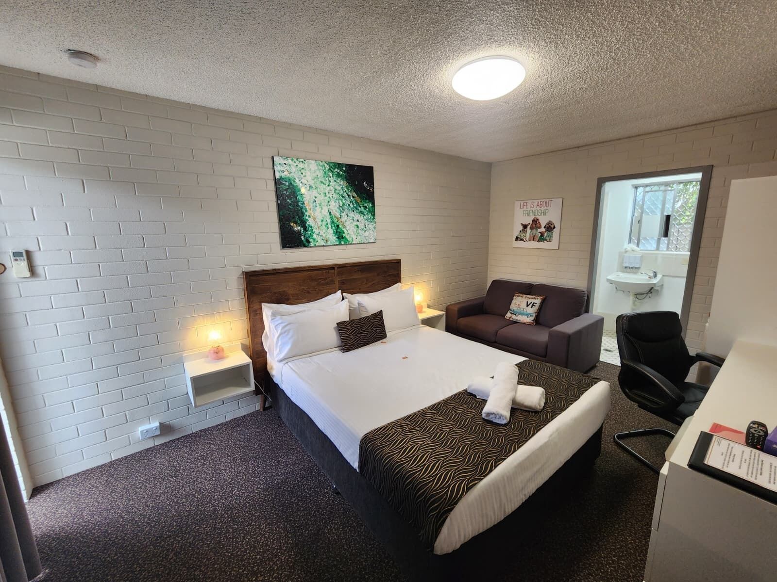 Habitación de hotel con cama, sofá, escritorio, silla, una mesita y una obra de arte colgada en la pared.