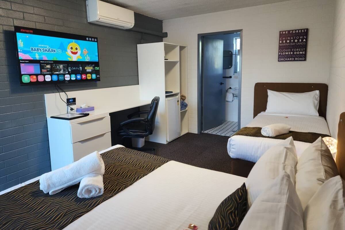 Habitación de hotel con televisor, escritorio, dos camas, armario y zona de ducha.