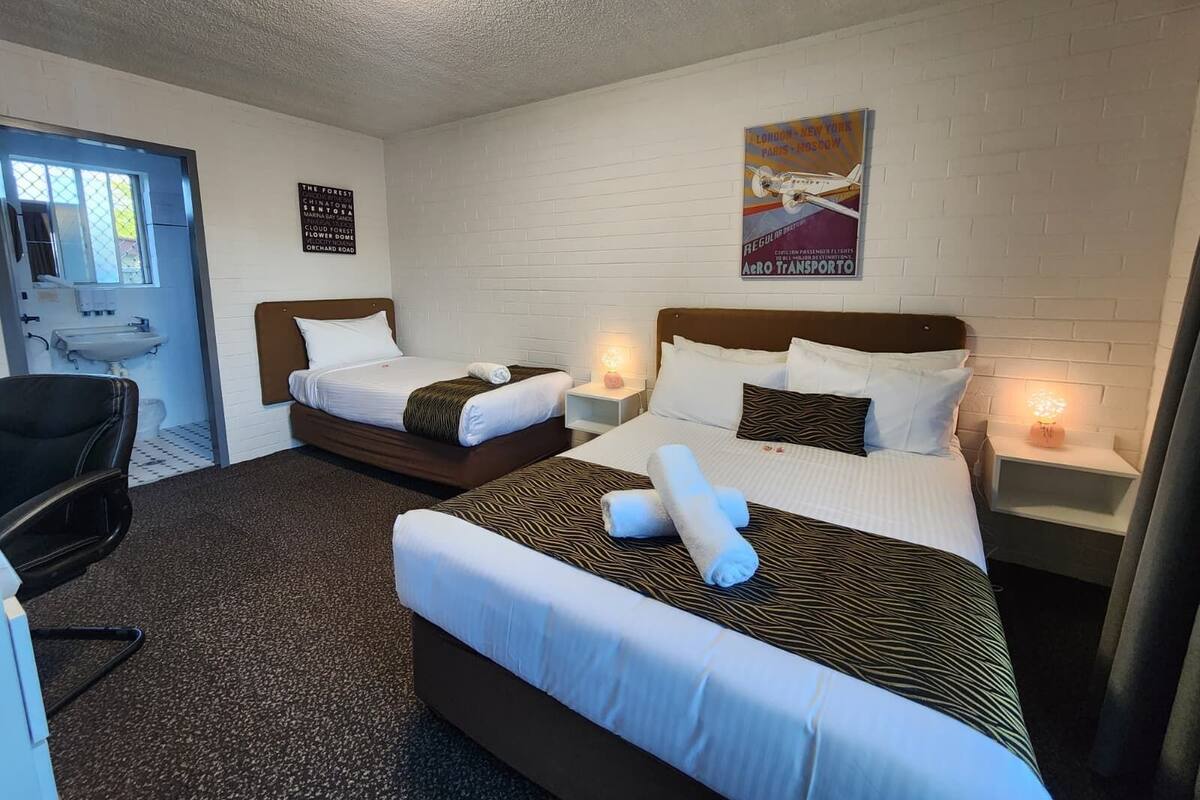Habitación de hotel con dos camas, un escritorio, una silla, un lavamanos y un cartel en la pared.
