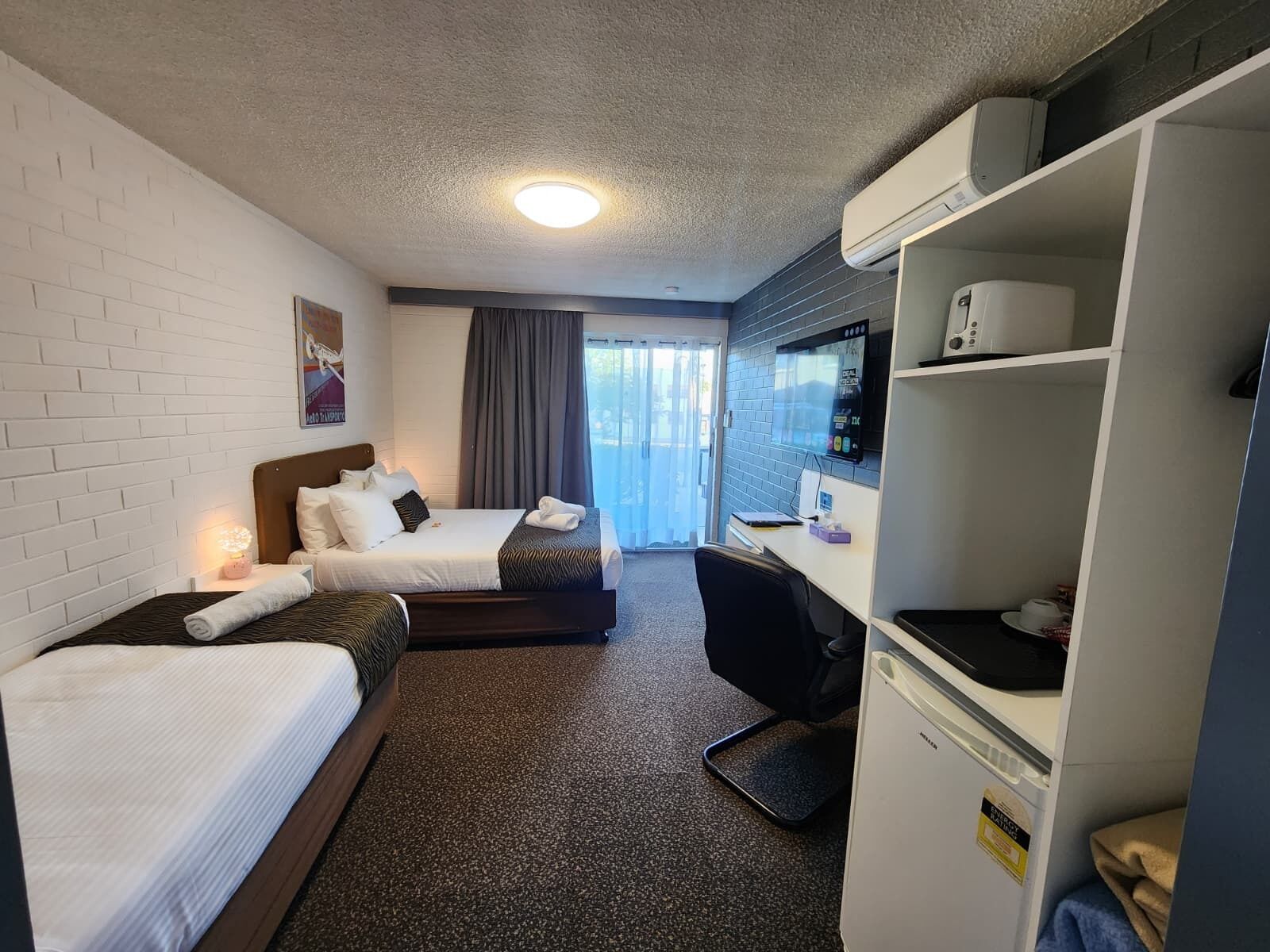 A hotel room with two beds, a desk, a chair, a wardrobe, and a window with curtains.