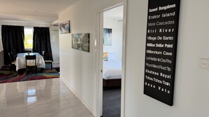 A hotel room with a bed, a dining area with a table and chairs, and a hallway with a black sign listing amenities. - Crest Motor Inn (Queanbeyan)