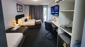 A hotel room with two beds, a desk with a computer, a chair, a TV, and an air conditioning unit. - Crest Motor Inn (Queanbeyan)