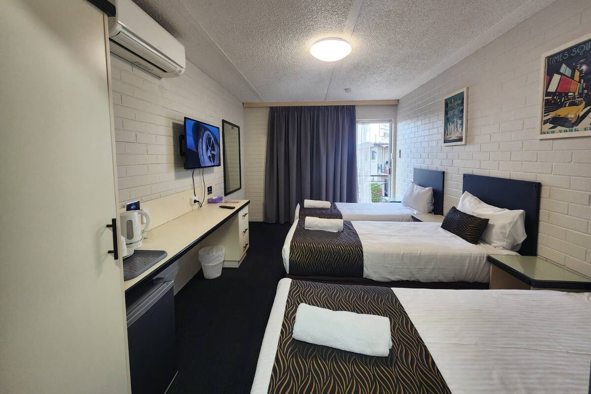 Habitación de hotel con dos camas, un televisor, un escritorio con hervidor y una ventana con cortinas.