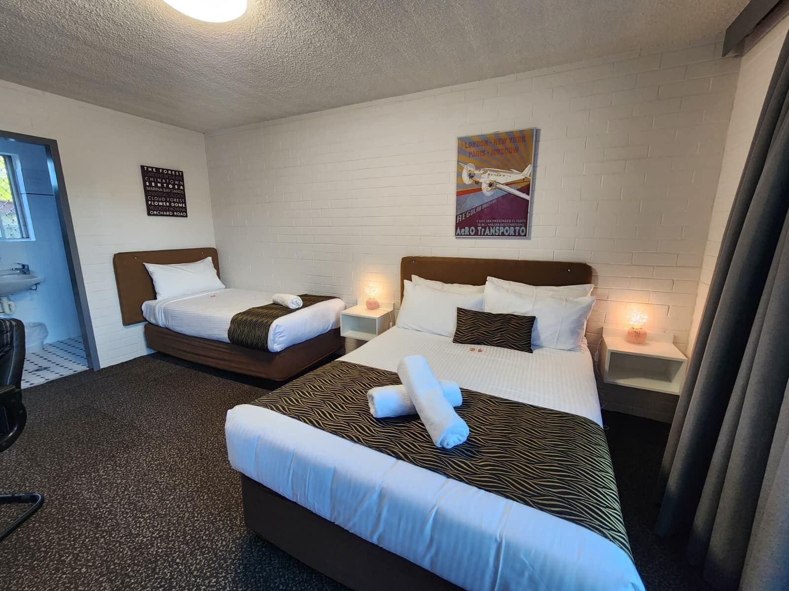 Ein Hotelzimmer mit zwei Betten, einer weißen Ziegelwand, einem Poster und einem Fenster.