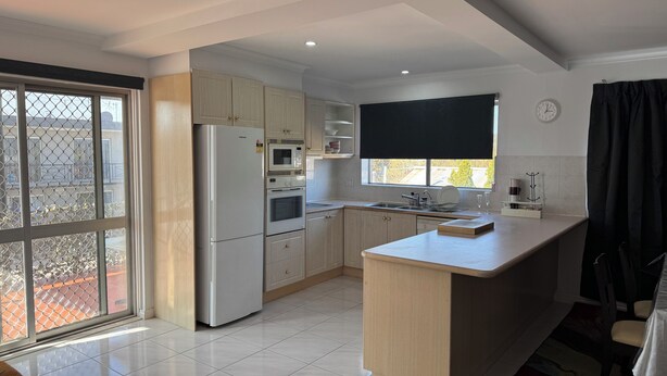 A modern kitchen with a central island, built-in appliances, and a large window. - Crest Motor Inn (Queanbeyan)