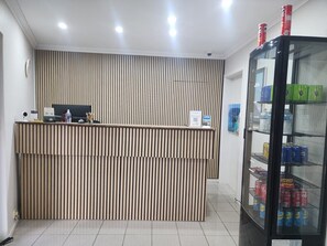 A reception desk with a vertical slat design, a computer, a sign indicating room number 6, and a refrigerator stocked with beverages.