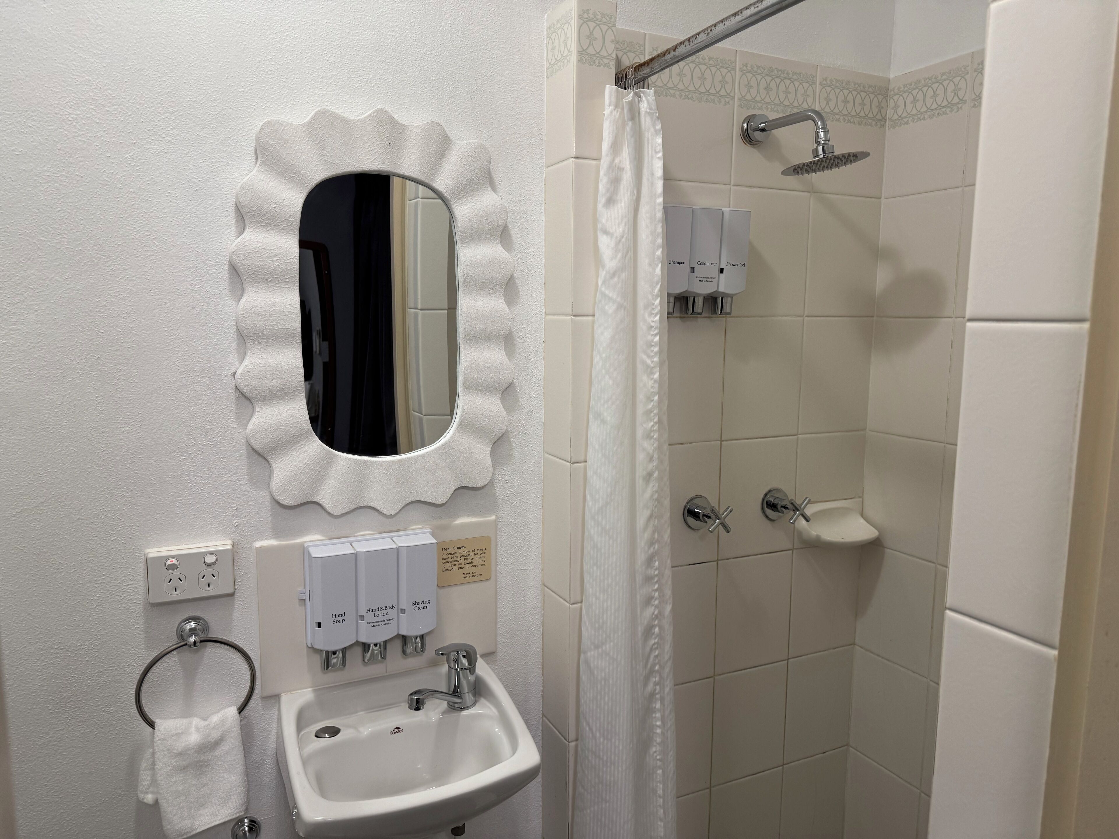 Un baño con lavamanos, espejo, ducha y dispensadores de gel antibacterial.