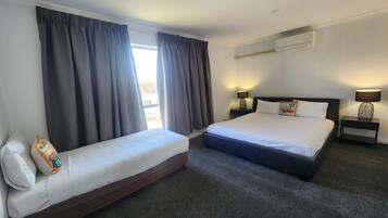 A hotel room with a double bed, a single bed, a nightstand with a lamp, and a window with curtains.