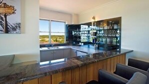 A modern kitchen with a bar area, wooden cabinets, and a view of the outdoors. - Tradewinds Apartments (Coffs Harbour)