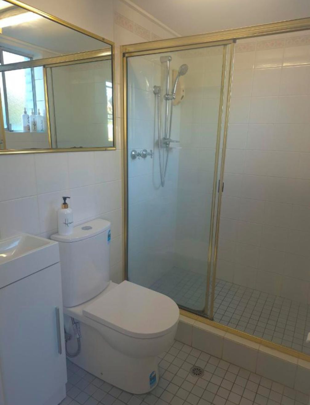 A bathroom with a toilet, a sink, a mirror, and a glass-enclosed shower area.