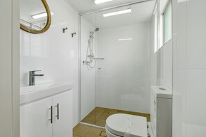 A modern bathroom with a shower, toilet, and vanity. - Tradewinds Apartments (Coffs Harbour)