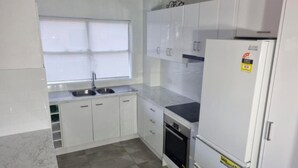 A kitchen with white cabinets, a sink, a stove, and a refrigerator. - Tradewinds Apartments (Coffs Harbour)