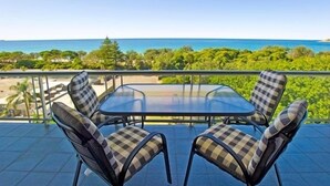 A balcony with a glass table and checkered chairs, overlooking a coastal landscape. - Tradewinds Apartments (Coffs Harbour)