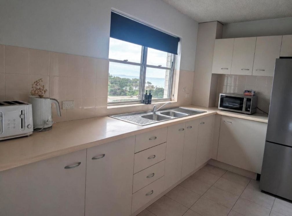A kitchen with a window, a toaster, a sink, a microwave, and a refrigerator.