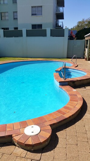 A swimming pool with a curved brick edge and a metal ladder. - Tradewinds Apartments (Coffs Harbour)
