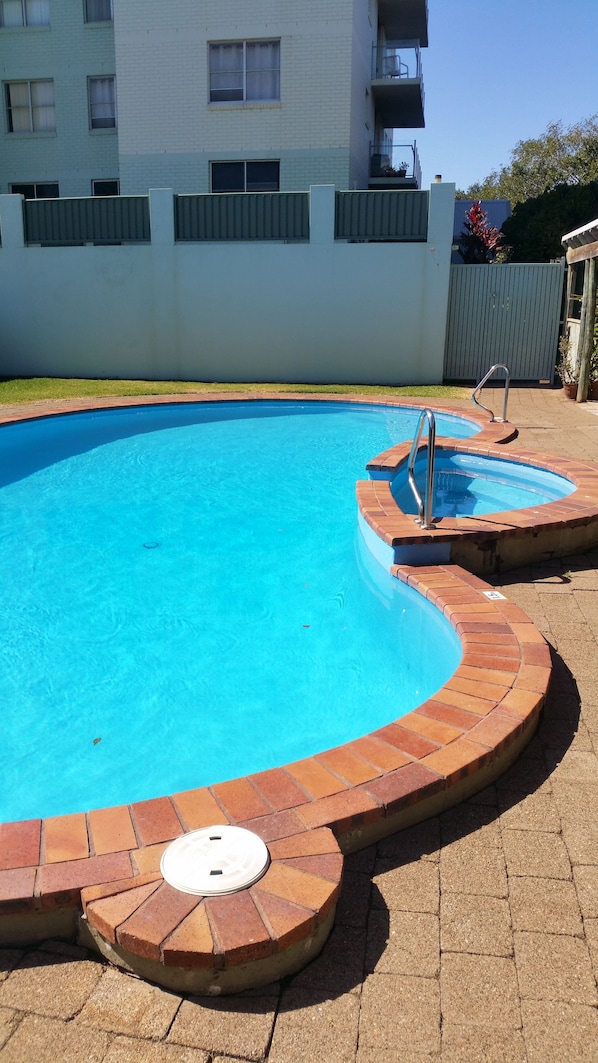 A swimming pool with a curved brick edge and a metal ladder. - Tradewinds Apartments (Coffs Harbour)