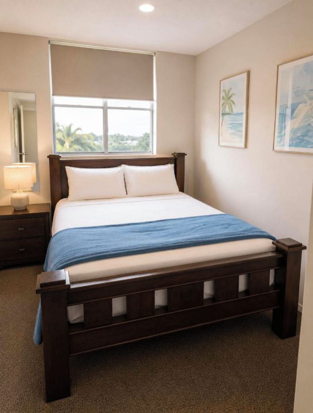 A bedroom with a bed, a nightstand, a lamp, and a window with a view.