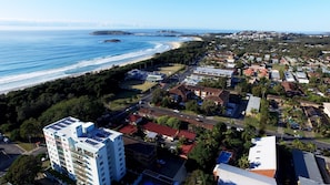 An aerial view of a coastal town with a beach, residential areas, and a prominent hotel with multiple floors and balconies. - Tradewinds Apartments (Coffs Harbour)