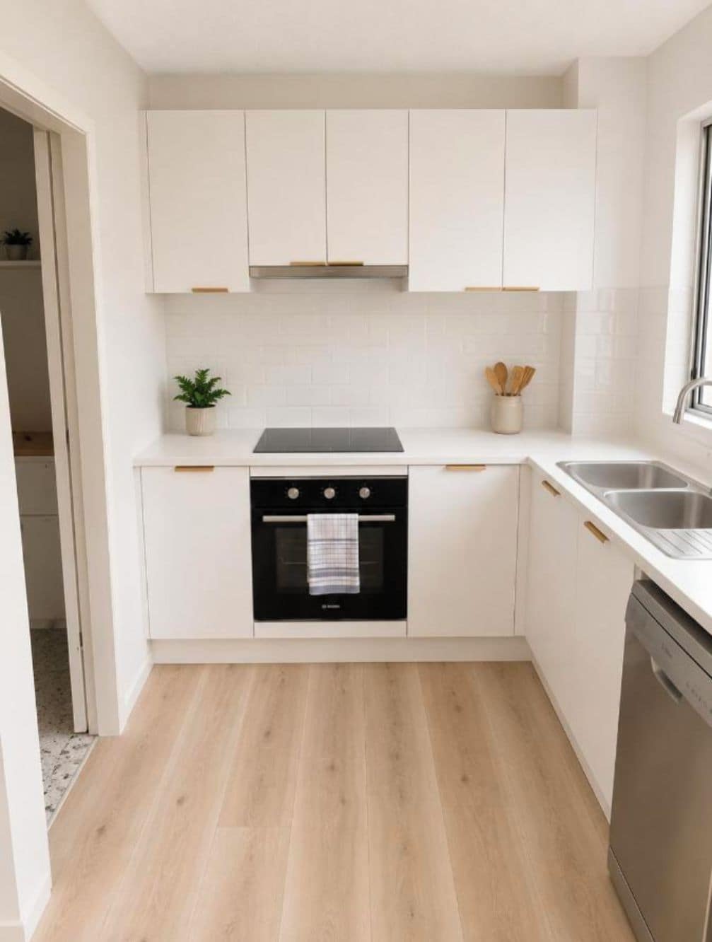 Una cocina compacta con armarios blancos, horno negro y pileta de acero inoxidable.