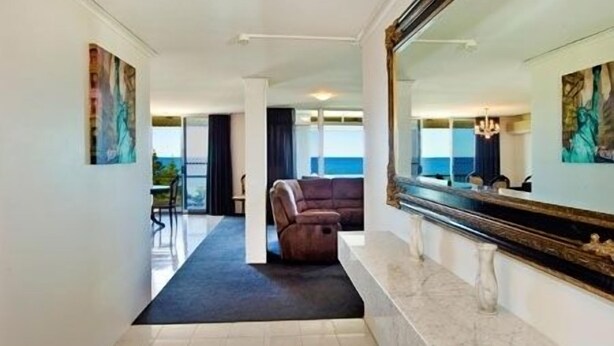 A modern hotel room with a large mirror, a sofa, and a view of the sea. - Tradewinds Apartments (Coffs Harbour)