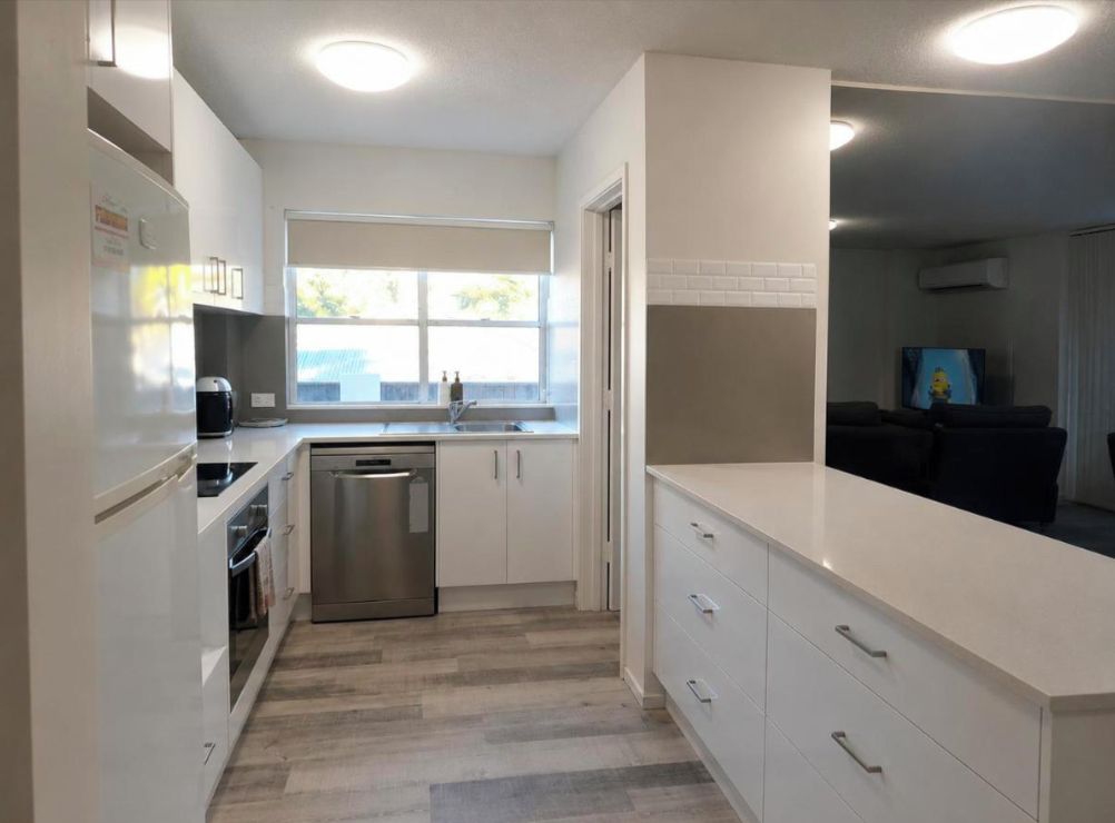 Una cocina moderna con armarios blancos, lavavajillas de acero inoxidable y un ventanal que proporciona luz natural.
