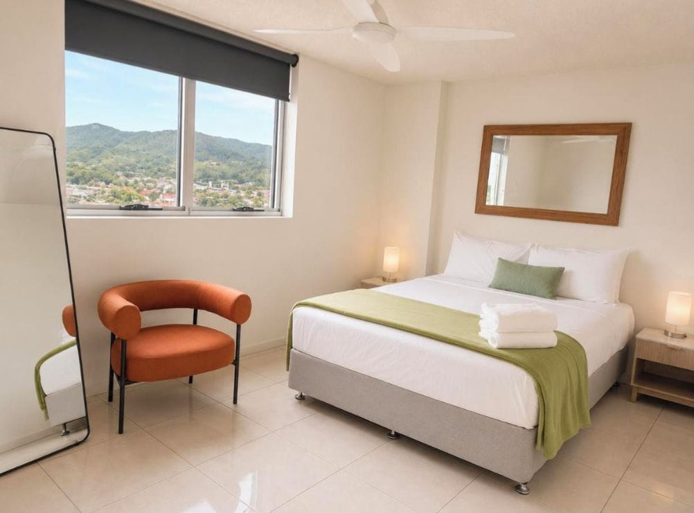 Una habitación de hotel con cama, una silla, un espejo, un ventanal con vistas y un ventilador de techo.