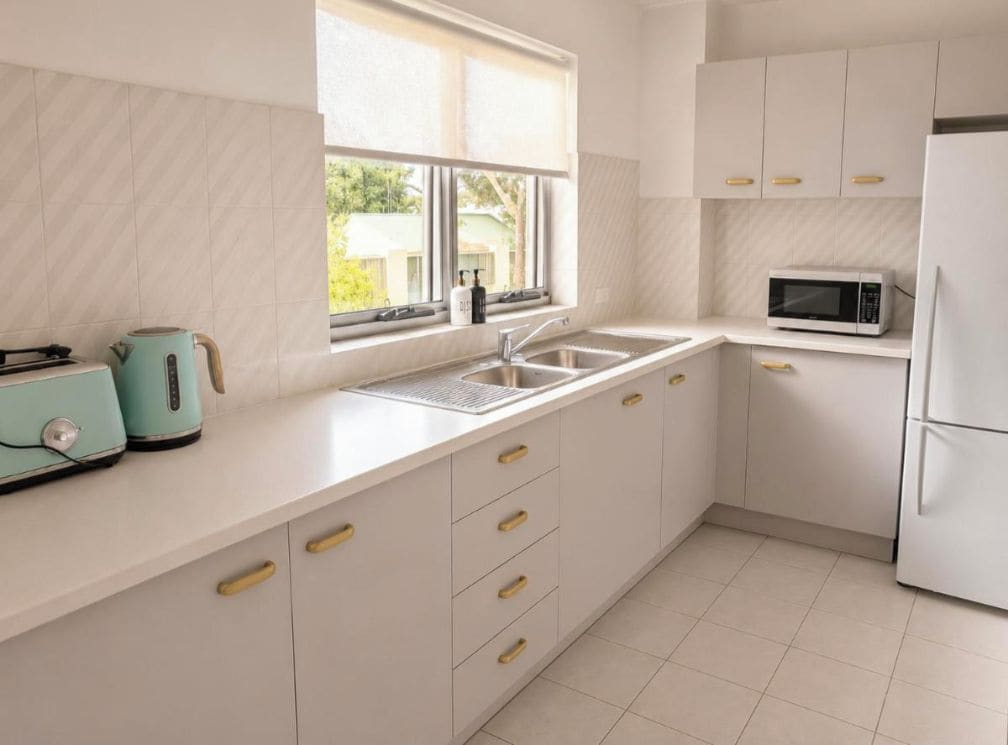 A modern kitchen with a sink, a microwave, and a kettle on the countertop.