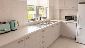 A modern kitchen with a sink, a microwave, and a kettle on the countertop.