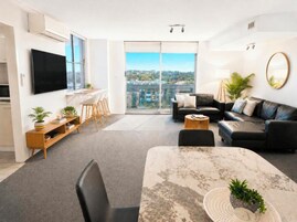 Una sala moderna con un televisor de pantalla plana, una mesa de comedor con sillas, un sofá y un ventanal con vistas a la ciudad.