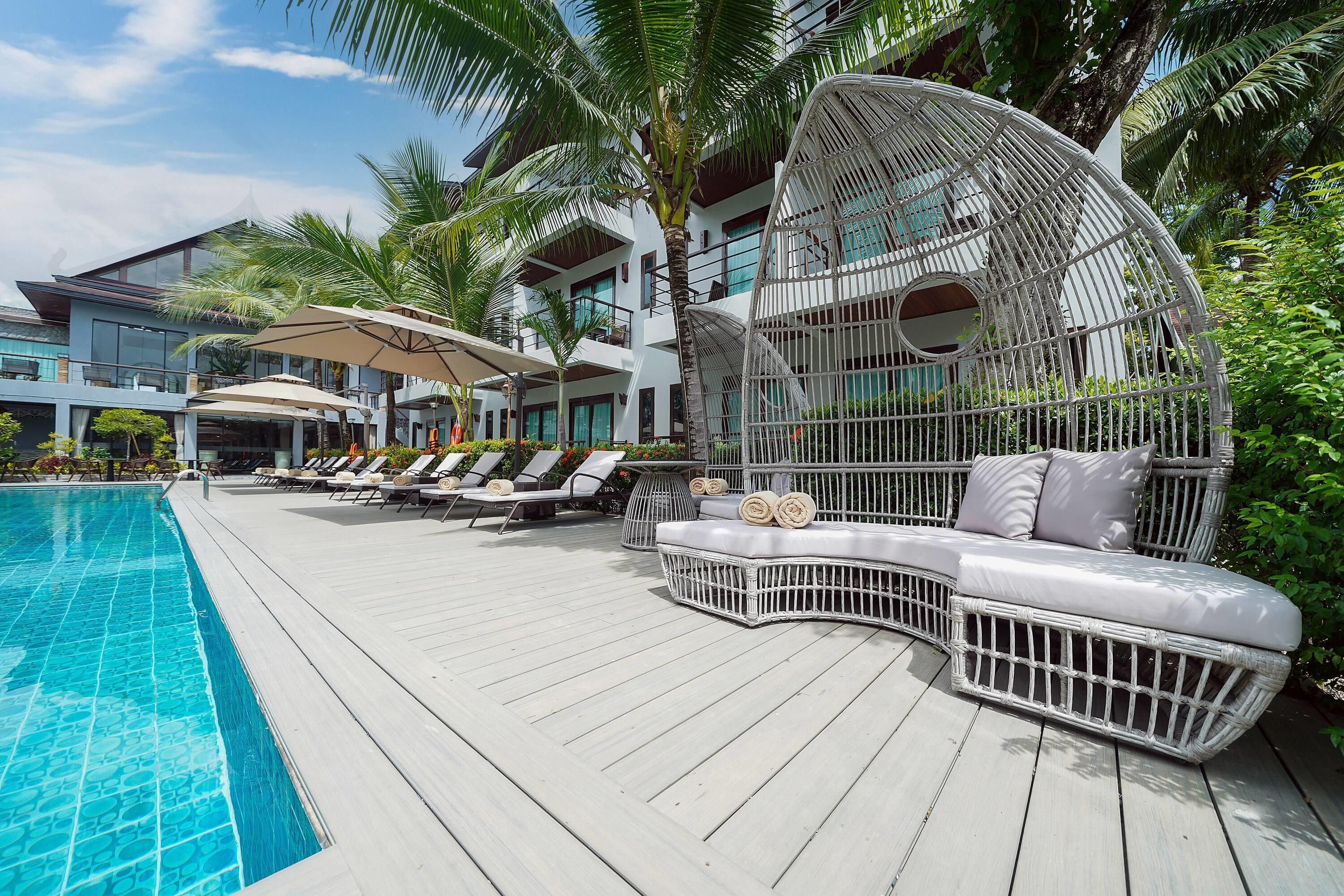 Un espace aménagé au bord de la piscine, avec des chaises longues, un canapé en osier blanc et un grand parasol.