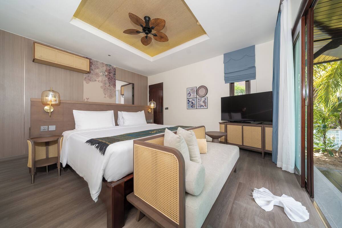 Una habitación de hotel moderna con una cama grande, un sofá, un televisor y un ventilador de techo.