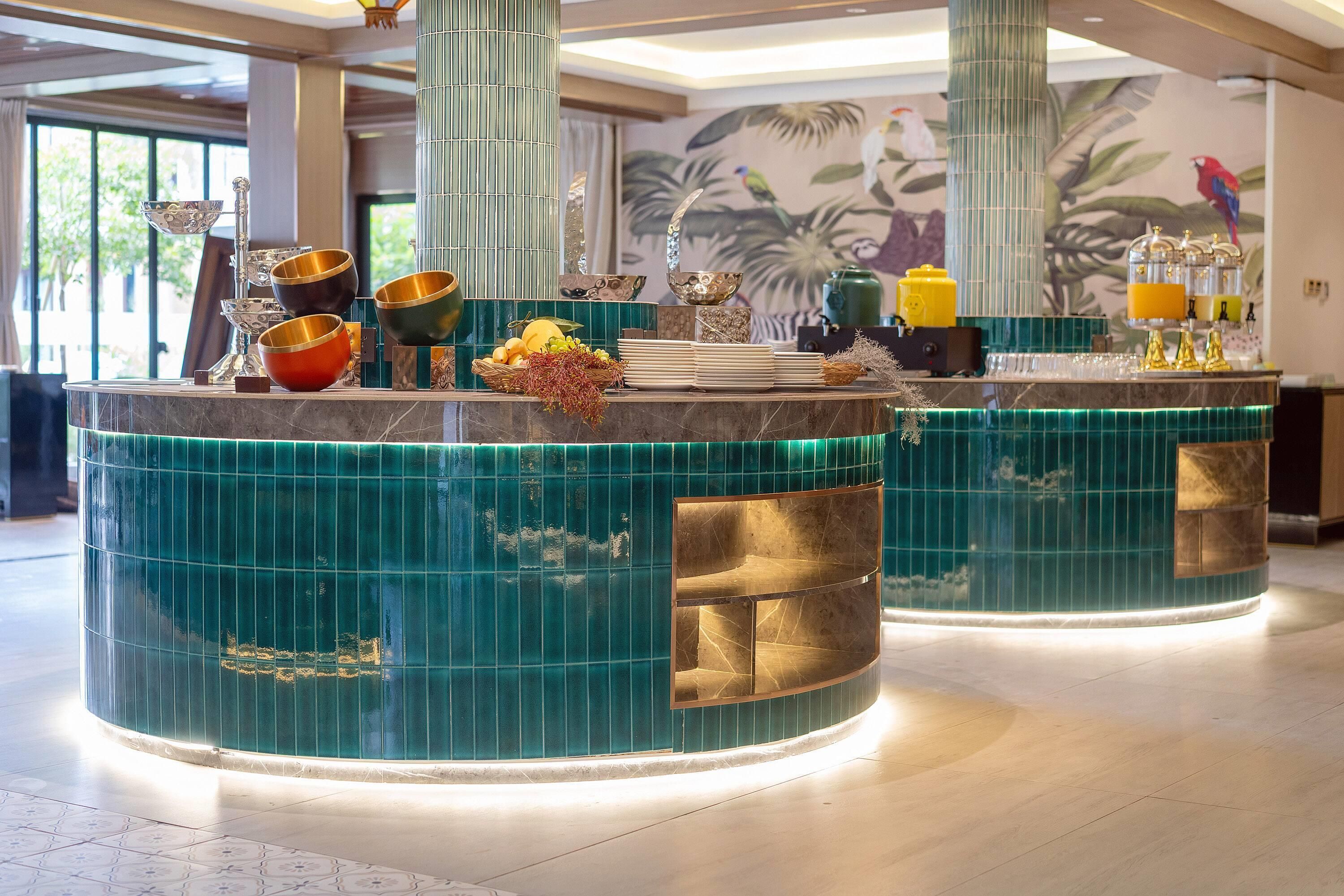 A bar area with a teal and gold color scheme, featuring a variety of glassware and a fruit display.
