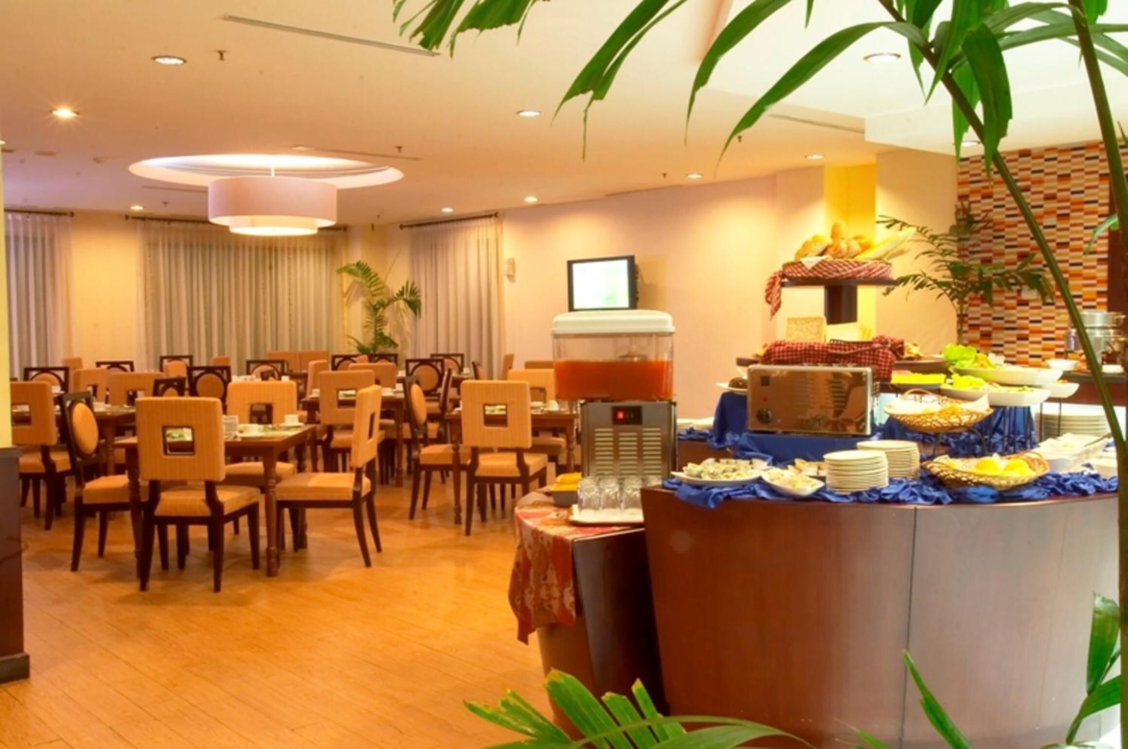 A dining area with multiple tables and chairs, a buffet with various food items, and a large plant in the foreground.