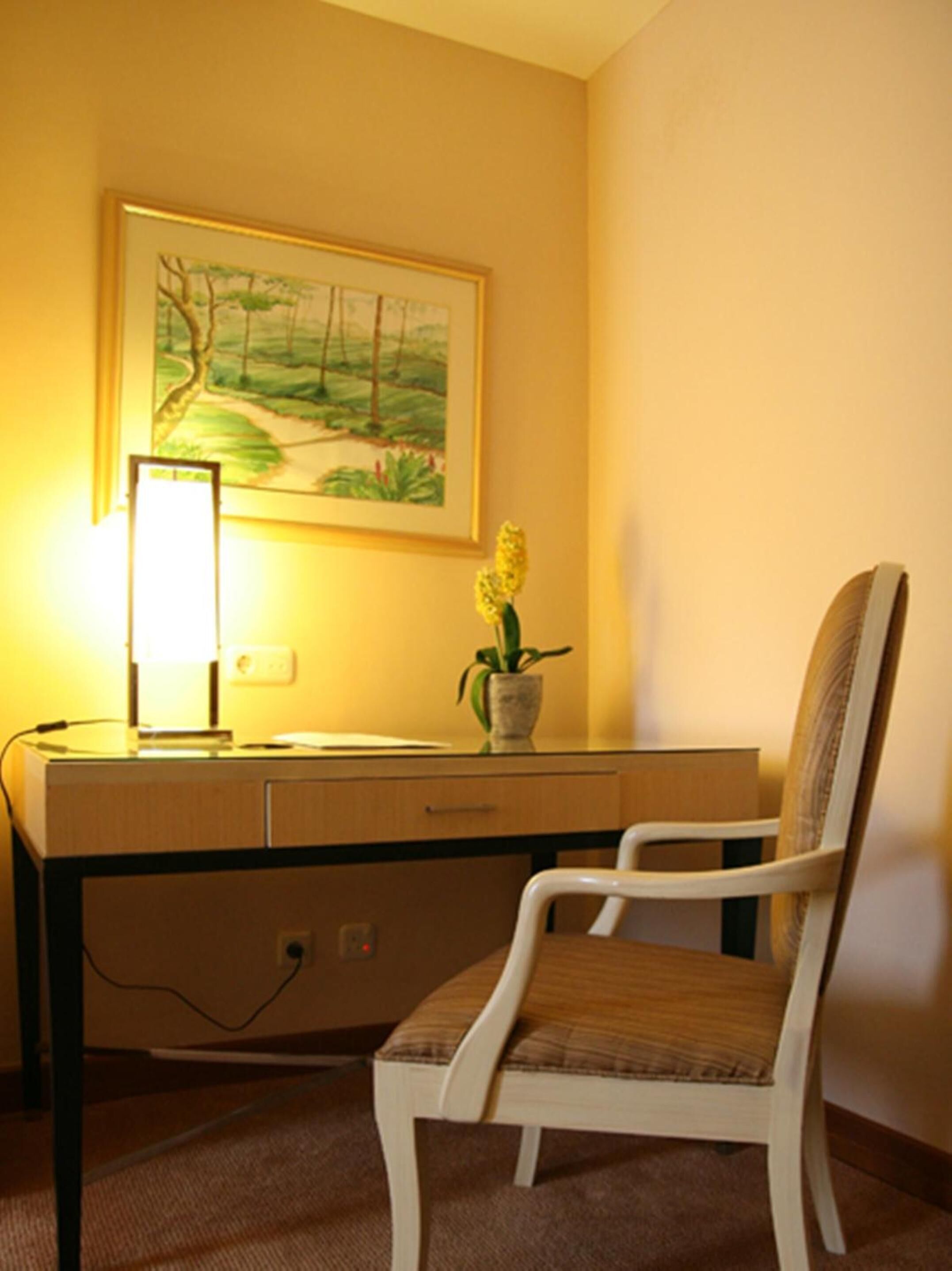 A desk with a lamp, a chair, and a painting on the wall.
