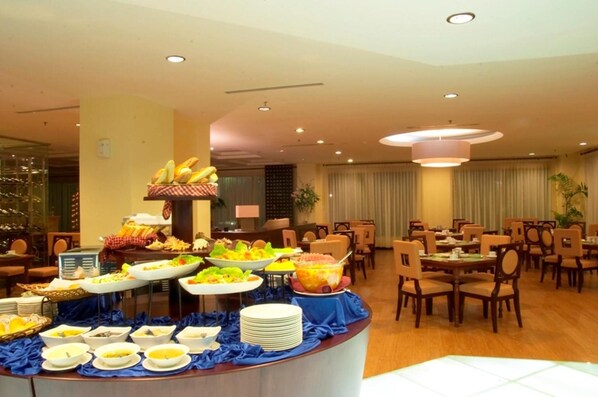 A buffet setup with various food items and a seating area with tables and chairs. - Hotel Gran Puri Manado (Manado)