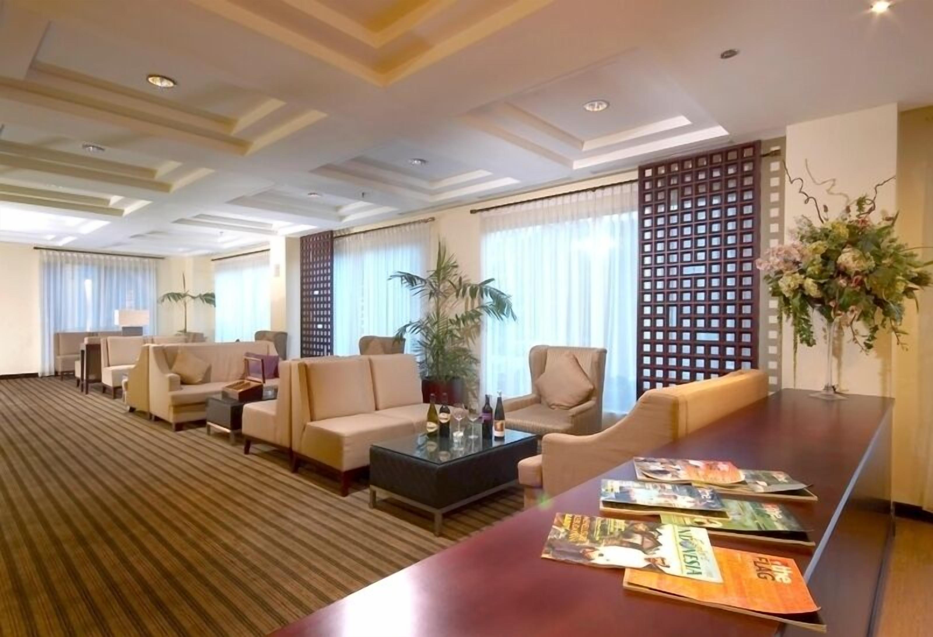Un hall de hotel con sofás, una mesa de centro, un mostrador de recepción y una planta decorativa.