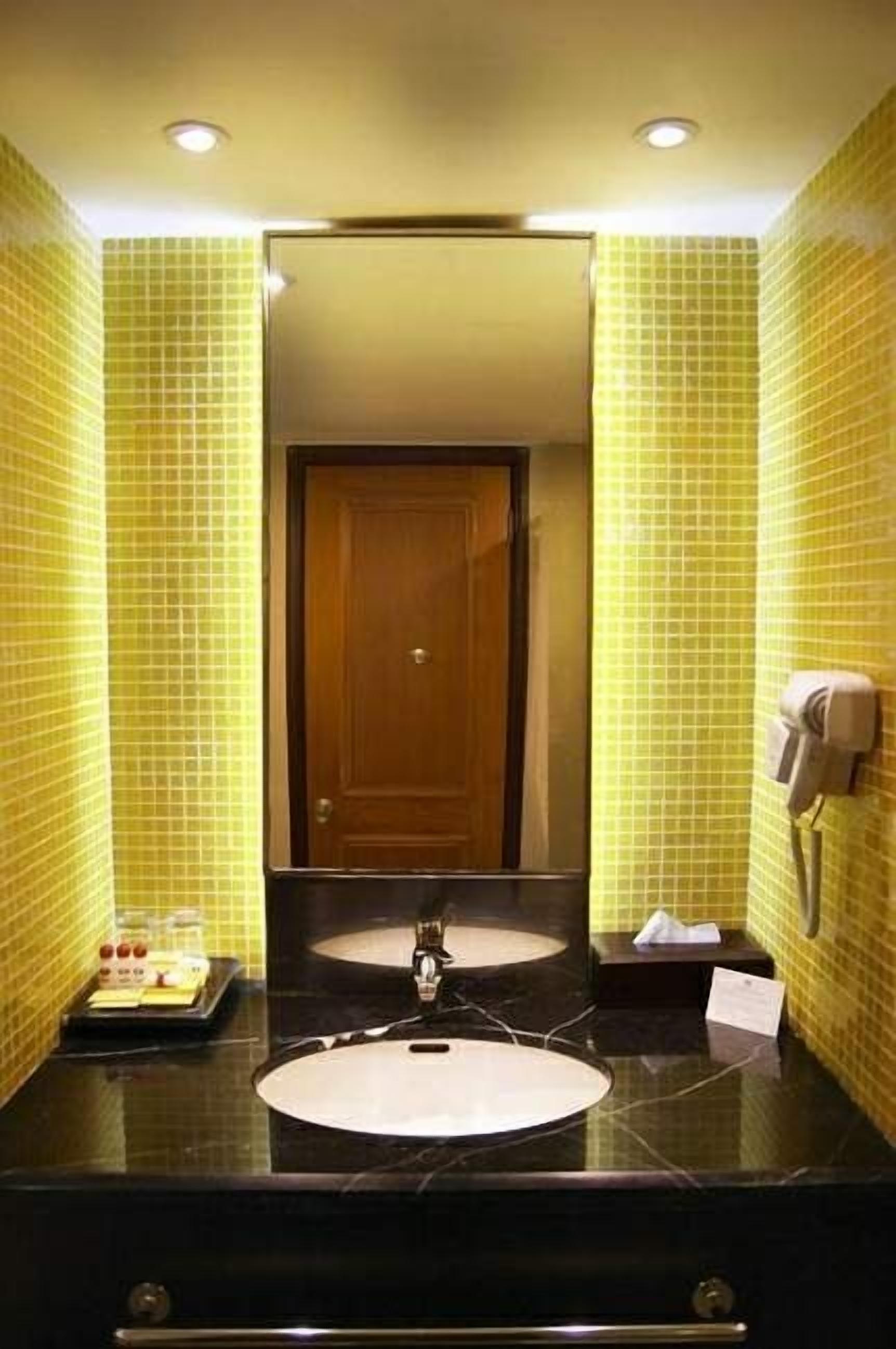 A bathroom with yellow tiled walls, a wooden door, a black marble sink, and a towel dispenser.