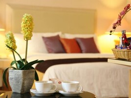 Una habitación de hotel con una cama, dos tazas de café sobre una mesa y un florero con flores.