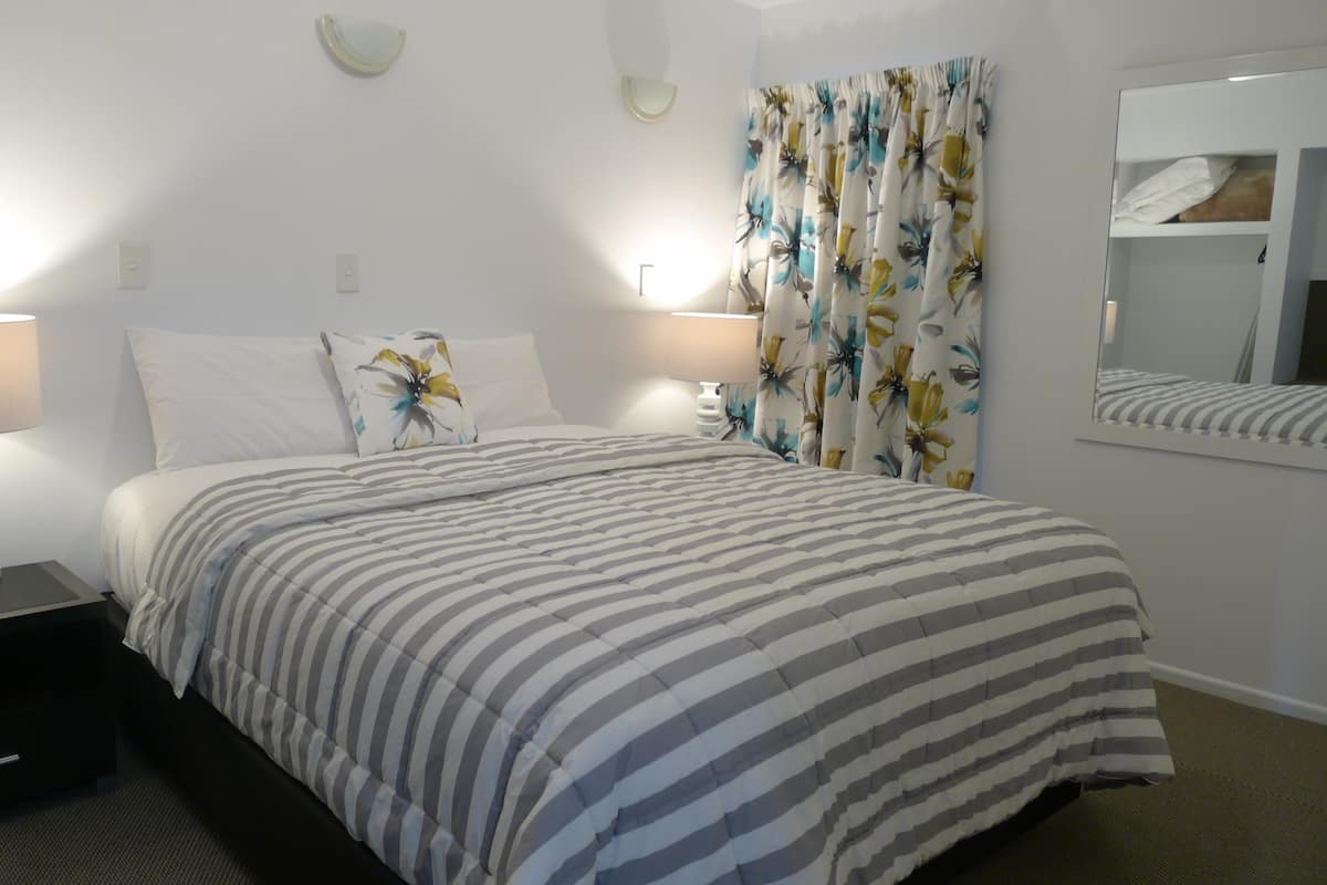 A neatly made bed with striped bedding, two bedside lamps, a nightstand, and a mirror above the bed.