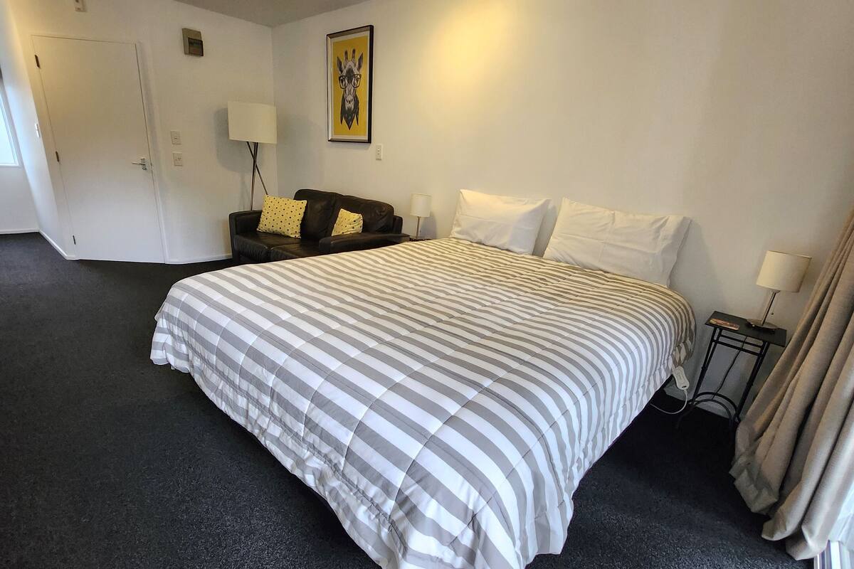 A hotel room with a large bed, a sofa, a lamp, and a painting on the wall.