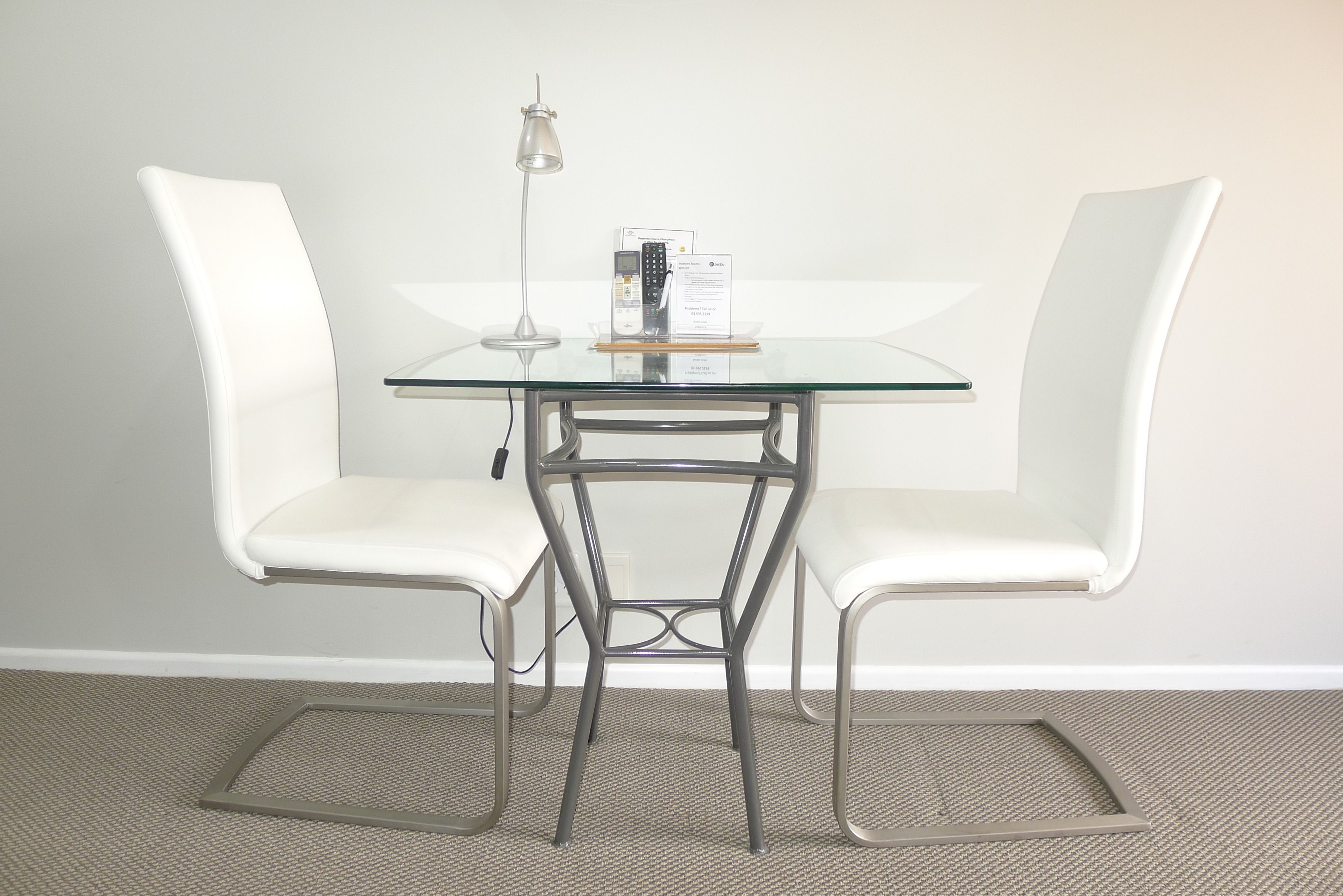 A modern, minimalist room with a glass table and two white chairs.