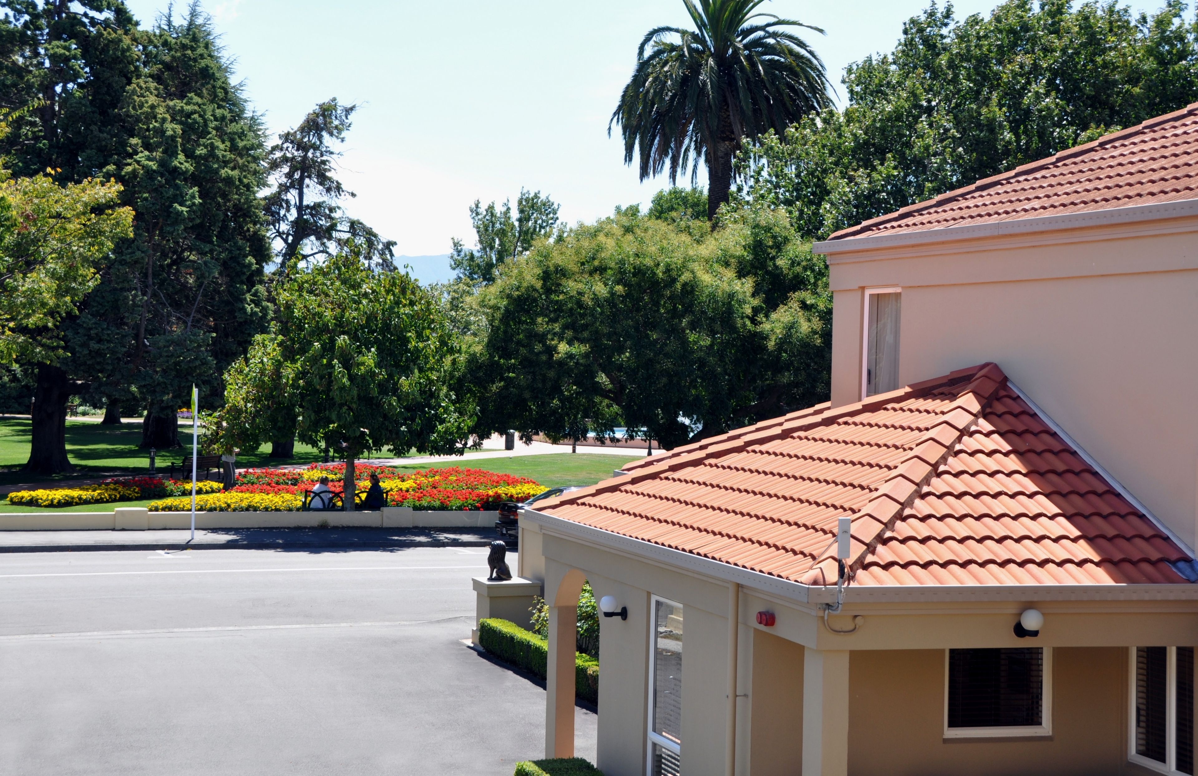 A building with a red-tiled roof, surrounded by greenery and a well-maintained garden with colorful flowers.
